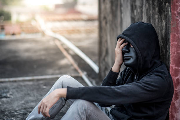istock Mystery man with black mask in headache gesture feeling stressed and depressed while sitting near grunge concrete wall in abandoned building 935571916