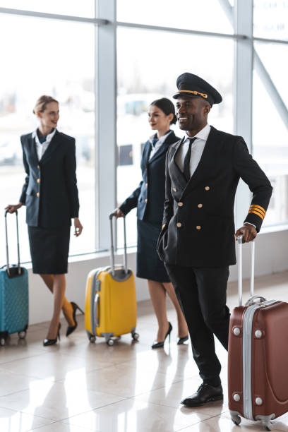 young pilot and stewardesses with luggage walking by airport - cabin crew pilot airport walking imagens e fotografias de stock