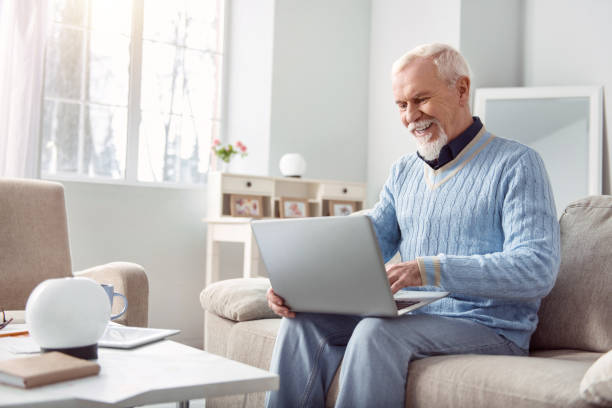 istock Upbeat senior man using his laptop in living room 935580402