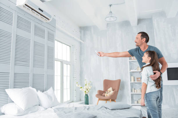 Positive joyful man holding a remote control Air conditioning. Positive delighted joyful man standing together with his daughter and looking at the air conditioner while holing a remote control air conditioner family stock pictures, royalty-free photos & images