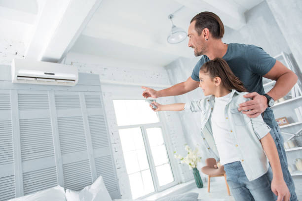 Positive joyful man pointing at the air conditioner Comfortable temperature. Positive happy joyful man standing near his daughter and pointing at the air conditioner while teaching her how to use it air conditioner family stock pictures, royalty-free photos & images