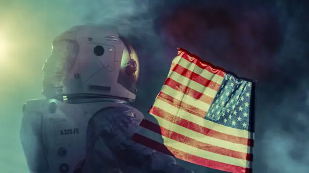 Photo of Strong Astronaut Walks Through the Storm with a Flag of Unites States of America, Proudly Plants it on the Dark Alien Planet. Space Travel, Colonisation Theme.