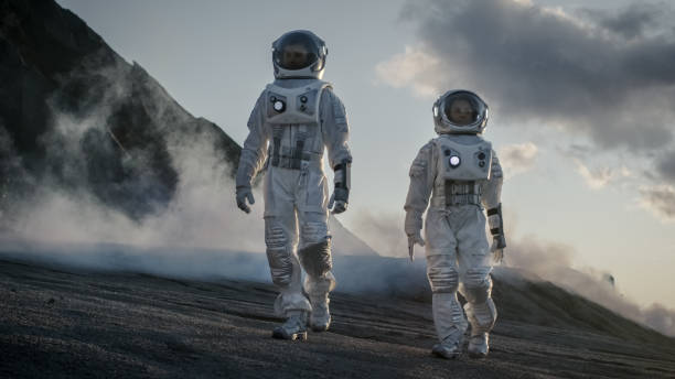 dois astronautas em trajes espaciais confiantemente caminhando planeta alienígena, exploração da superfície do planeta. na base de pesquisa de fundo / estação e rover. viagens espaciais, conceito de colonização. - colonization - fotografias e filmes do acervo