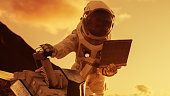 Astronaut in the Space Suit Works on Laptop, Adjusting Rover on a New Alien Red Planet, Presumably Mars. Day Light High-Tech Space Exploration, Mission, Discovering and Colonizing Habitable Planets.