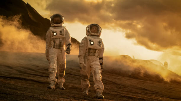 istock Two Astronauts in Space Suits Confidently Walking on Mars, Exploration Expedition on the Planet's Surface. Red Planet Covered in Rocks, Gas and Smoke. Humans Overcoming Difficulties. 935640318