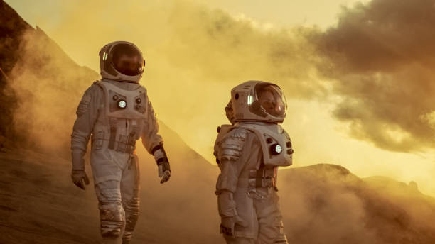 istock Two Astronauts in Space Suits Confidently Walking on Mars, Exploration Expedition on the Planet's Surface. Red Planet Covered in Rocks, Gas and Smoke. Humans Overcoming Difficulties. 935640320