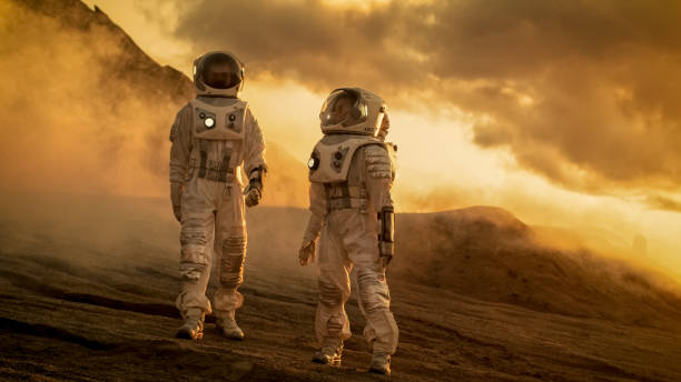 Two Astronauts in Space Suits Confidently Walking on Mars, Exploration Expedition on the Planet's Surface. Red Planet Covered in Rocks, Gas and Smoke. Humans Overcoming Difficulties.