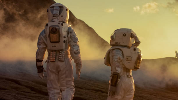 istock Two Astronauts in Space Suits Confidently Walking on Mars, Exploration Expedition on the Planet's Surface. Red Planet Covered in Rocks, Gas and Smoke. Humans Overcoming Difficulties. 935640346