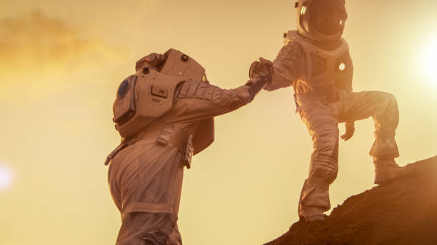 Two Astronauts Climbing Mountain Hill Helping Each Other, Reaching the Top. Helping Hand. Overcoming Difficulties, Important Moment for the Human Race.