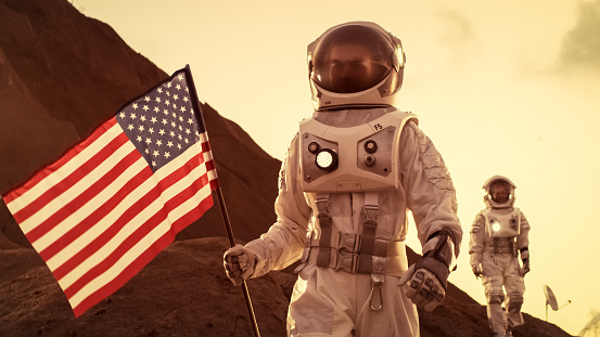 Two Astronauts Explore Mars/ Red Planet. One Cosmonaut Carries American Flag. Technological Advance Brings Space Exploration, Travel, Colonization Concept.