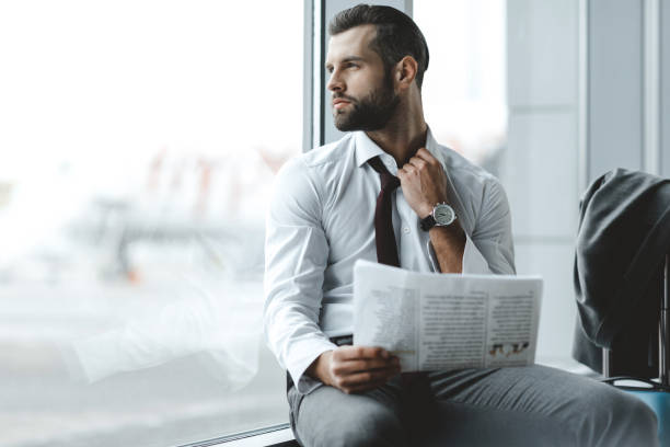 istock handsome young businessman through window while waiting for flight at airport lobby 935640590