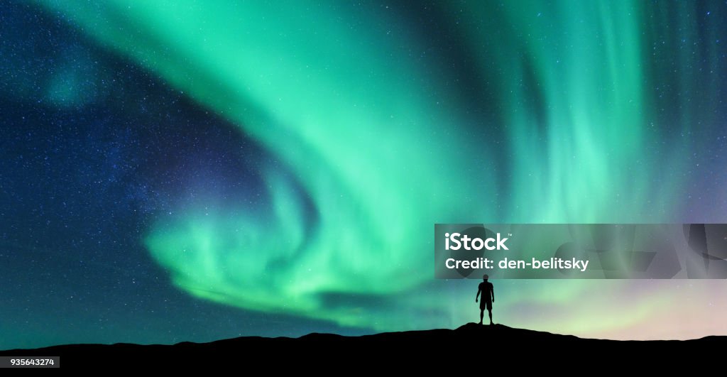 Aurora borealis and silhouette of standing man Aurora borealis and silhouette of standing man. Lofoten islands, Norway. Aurora and happy man. Sky with stars and green polar lights. Night landscape with aurora and people. Concept. Nature background Aurora Borealis Stock Photo
