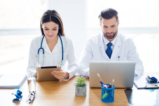 istock Two doctors colleagues are sitting at the work place and using modern technology for their work, in white coats, focused 935659616