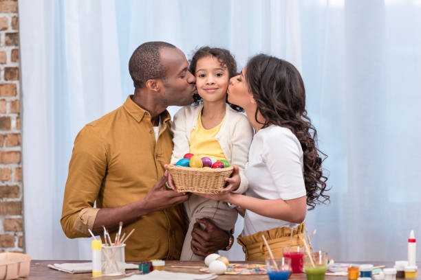 アフリカ系アメリカ人の両親が娘とイースターエッグと持株ストロー バスケットにキス - easter egg 写真 ストックフォトと画像