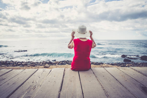 Senior woman with sun hat and red dress on the beach in Tenerife, Playa de las Americas, Spain. Europe. No logos. Nikon d850.