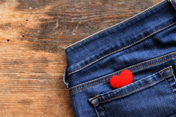 Small red heart in jeans pocket on wooden table