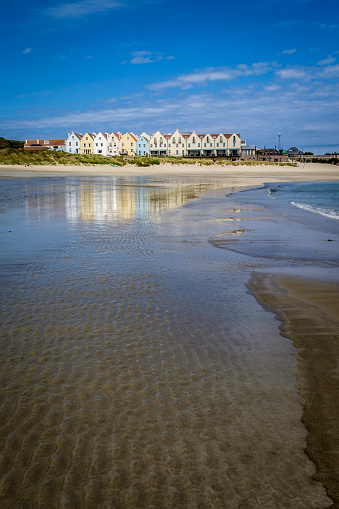 Row of houses and a hotel, reflected in the water at Braye Beach, Alderney, Guernsey, Channel Islands