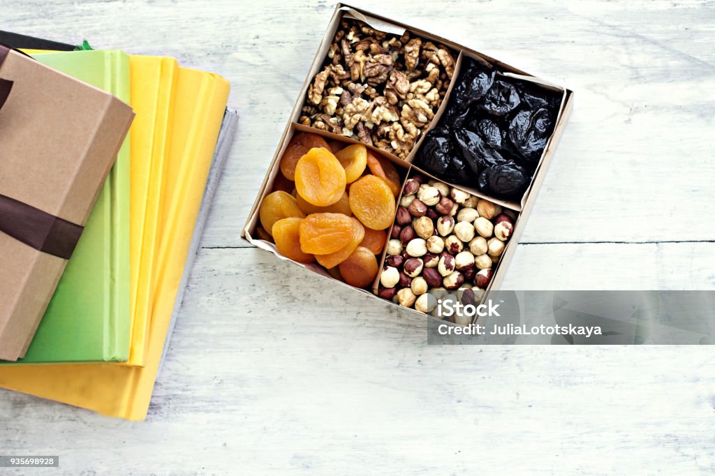 A box of nuts and dried fruits and a stack of books. A box of nuts and dried fruits and a stack of books. Dried apricots, prunes, walnuts, hazelnuts. Snack Stock Photo