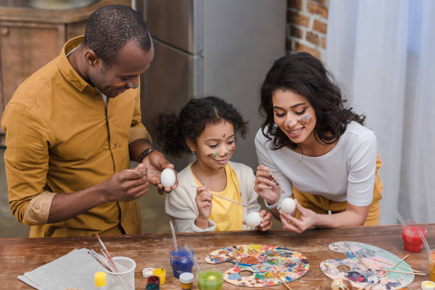 vista de alto ângulo de pais americanos africano e filha pintar ovos de páscoa - two generation family holiday vacations easter egg - fotografias e filmes do acervo