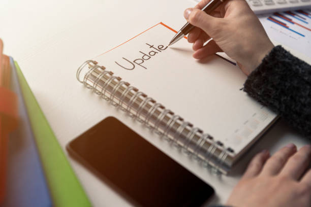 istock Womans hand writing word update in a notebook on a desk. Project update checklist. Notebook, pen and books. System update 935705416