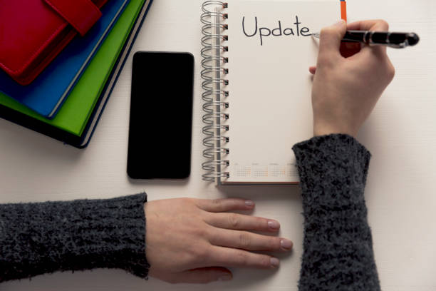 istock Womans hand writing word update in a notebook on a desk. Project update checklist. Notebook, pen and books. System update 935705442