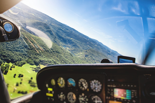 Small airplane cockpit interior in selective focus with control instrument panel and hilly landscape background in summer