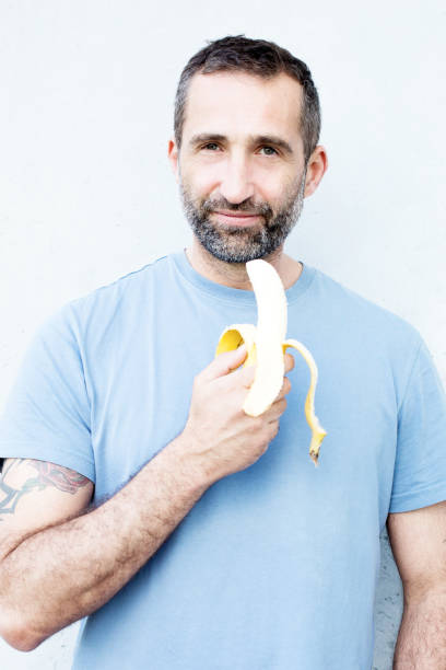 handsome bearded man eating a banana - stubble men tattoo sensuality imagens e fotografias de stock