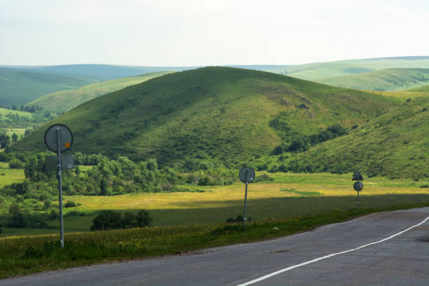 Landscape with road sign along highway on foreground and hills on background.