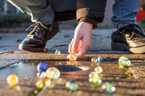 Child playing with marbles on yhe sidewalk. old-fashioned toys still in use today.