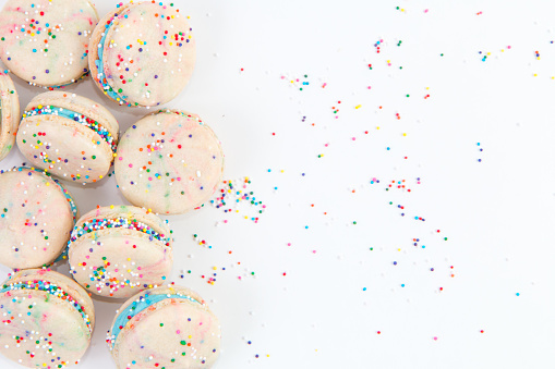 Birthday cake flavored macarons with blue icing and colorful sprinkles isolated on a white seamless background.