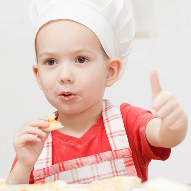 istock Little cheerful boy chef cooks and eats pizza 935770798
