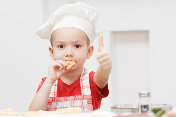 istock Little cheerful boy chef cooks and eats pizza 935770810
