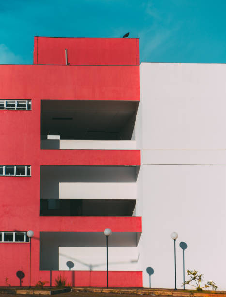 The facade of the modern building divided into two: one part of the facade is red and has balconies and windows, another part is white; lanterns below, a huge bird on the roof, minimalist geometry