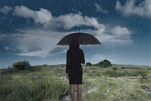 Businesswoman standing with an umbrella in rain over dark sky background