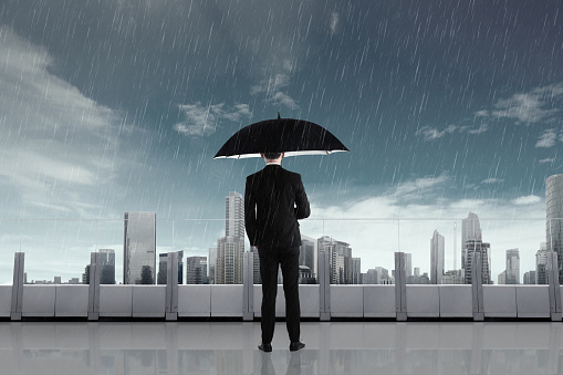 Businessman in the rain with umbrella looking at city view