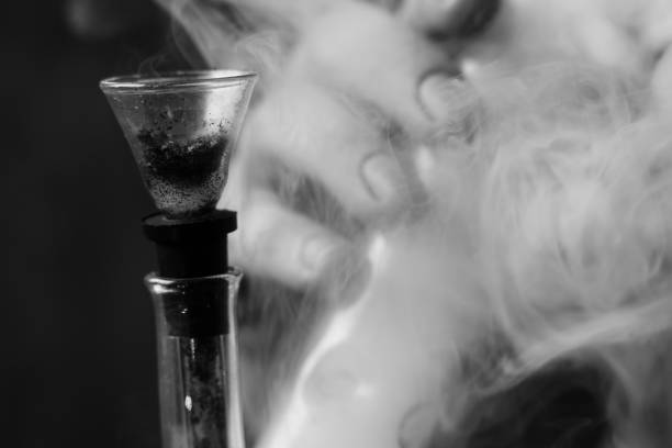 istock A man smokes cannabis weed, a bong and a lighter in his hands. Smoke on a black background. Concepts of medical marijuana use and legalization of the cannabis. Black and white 935824640