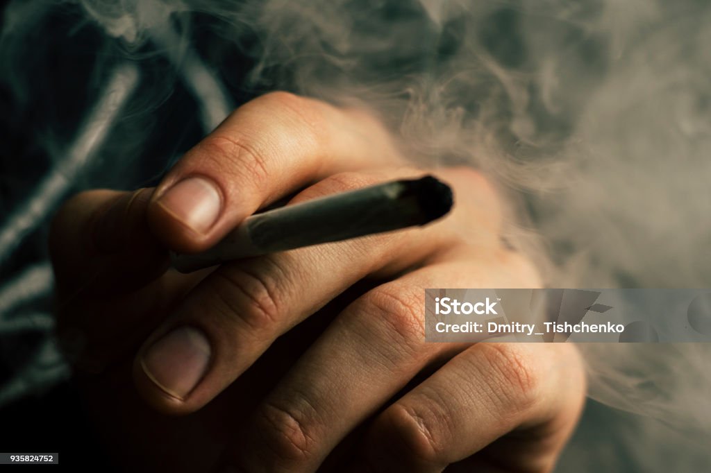 cannabis weed, a joint in his hands A man smokes . Smoke on a black background. Concepts of medical marijuana use and legalization of the cannabis. cannabis weed, a joint in his hands A man smokes . Smoke on a black background. Concepts of medical marijuana use and legalization of the cannabis. On a black background Addiction Stock Photo