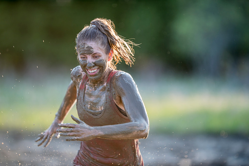 A Caucasian woman is outdoors on a sunny day. She is participating in a mud run. The woman is covered in dirt.
