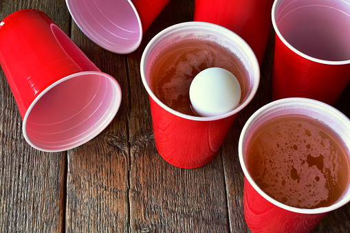 A close up image of red plastic beer pong cups filled with beer.