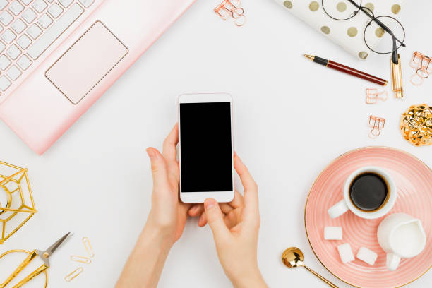istock Stylish flatlay frame arrangement with woman's hands holding white smartphone with black copyspace, pink laptop, coffee, planner and other accessories. Feminine business mockup 935836976