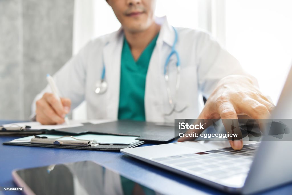Asian male Doctor is working. Young Asian male Doctor thinking and working with laptop at a hospital. Medical and health care concept. Stethoscope. Clipboard. Concentration. Doctor Stock Photo