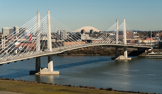 It's a clear day in Portland Oregon at Tilikum Crossing as people traverse the river with Mount St. Helens in the background