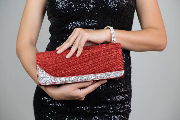 młoda kobieta w czarnej eleganckiej sukience kobiety trzymającej czerwoną diamentową luksusową torebkę na szarym tle. modne akcesoria. - clutch bag zdjęcia i obrazy z banku zdjęć