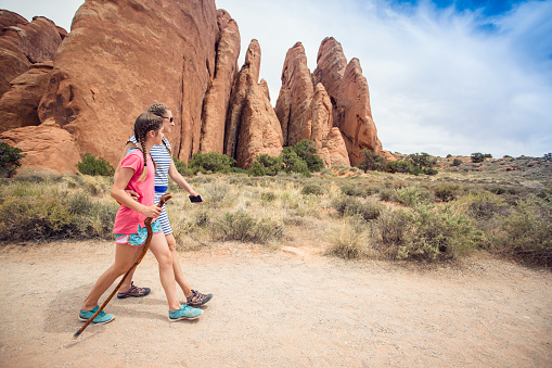 Two happy girls hiking together in the beautiful rock cliffs of Arches National Park. Walking along a scenic trail with large rock formations in the background