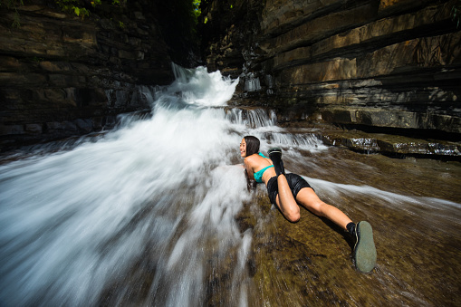 A young happy Japanese woman laying down enjoying the water that is flowing fast down a rocky river. Water is blurry from use of a slow shutter speed to show movement.