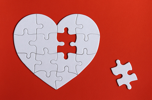 A missing piece of the puzzle and puzzles in the shape of a white heart on the red background.