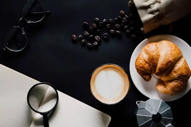 Latte art ,Croissant ,book,glasses and moka pot with Roasted coffee on black background in the morning top view and instagram style filter photo vintage tone