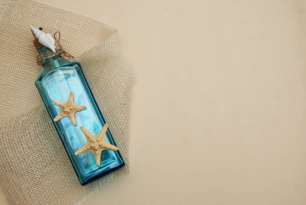 istock Nautical Theme Backdrop, Decorative Bottle with Shells, Starfish on Neutral Ivory Background. Place for text. Selective focus. 935919444