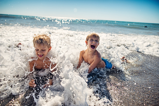Brothers are having fun in sea in Bibbona, Tuscany. Kids aged 7 are lying on the beach and being splashed by waves. Boys are laughing and screaming.\nNikon D800