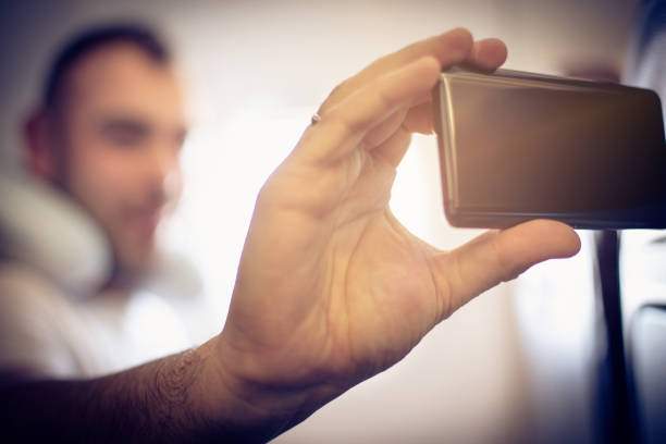 Man taking self portrait in airplane. Focus is on hand. Close up. Space for copy.